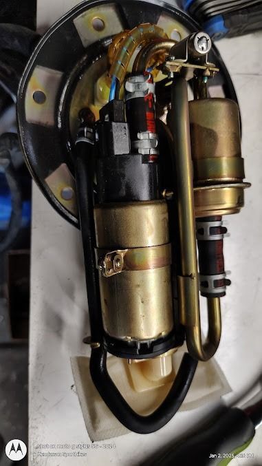 Close-up of a mechanical fuel pump assembly with gold and black metal parts mounted on a white surface.