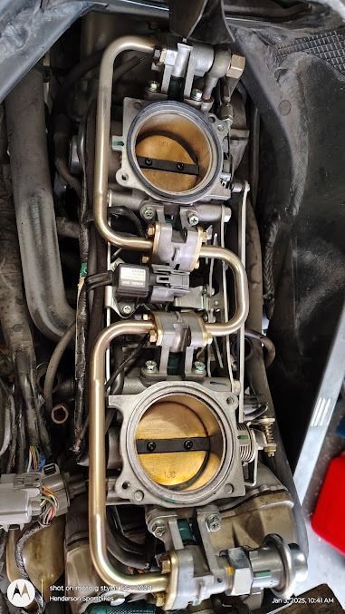 Two motorcycle carburetors with yellow throttle plates and visible fuel lines in an engine bay