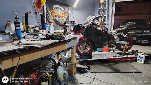 Cluttered workshop with a red sport motorcycle on a red stand, tools and equipment scattered around.