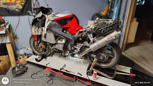 Red and black sport motorcycle on a workbench in a garage, with tools and cables around it