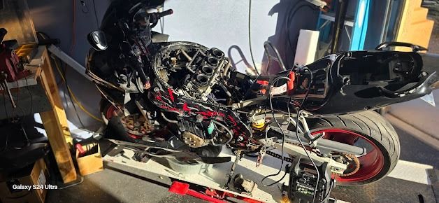 Damaged black motorcycle on a tow truck platform, with exposed engine and bent frame.
