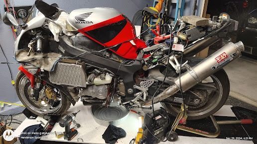 Red and silver racing motorcycle on a workshop stand with exposed mechanical parts and tools nearby