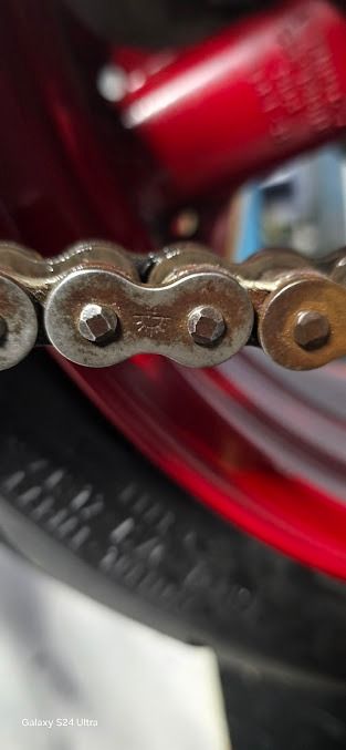 Close-up of a rusty bicycle chain on a red wheel rim and tire.