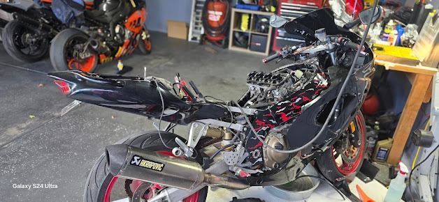 Damaged black-and-red motorcycle in a garage, with parts scattered around it.