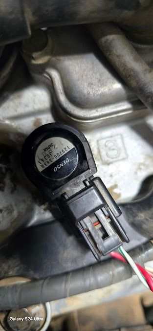 Close-up of a black electrical connector and sensor on a metal engine part.