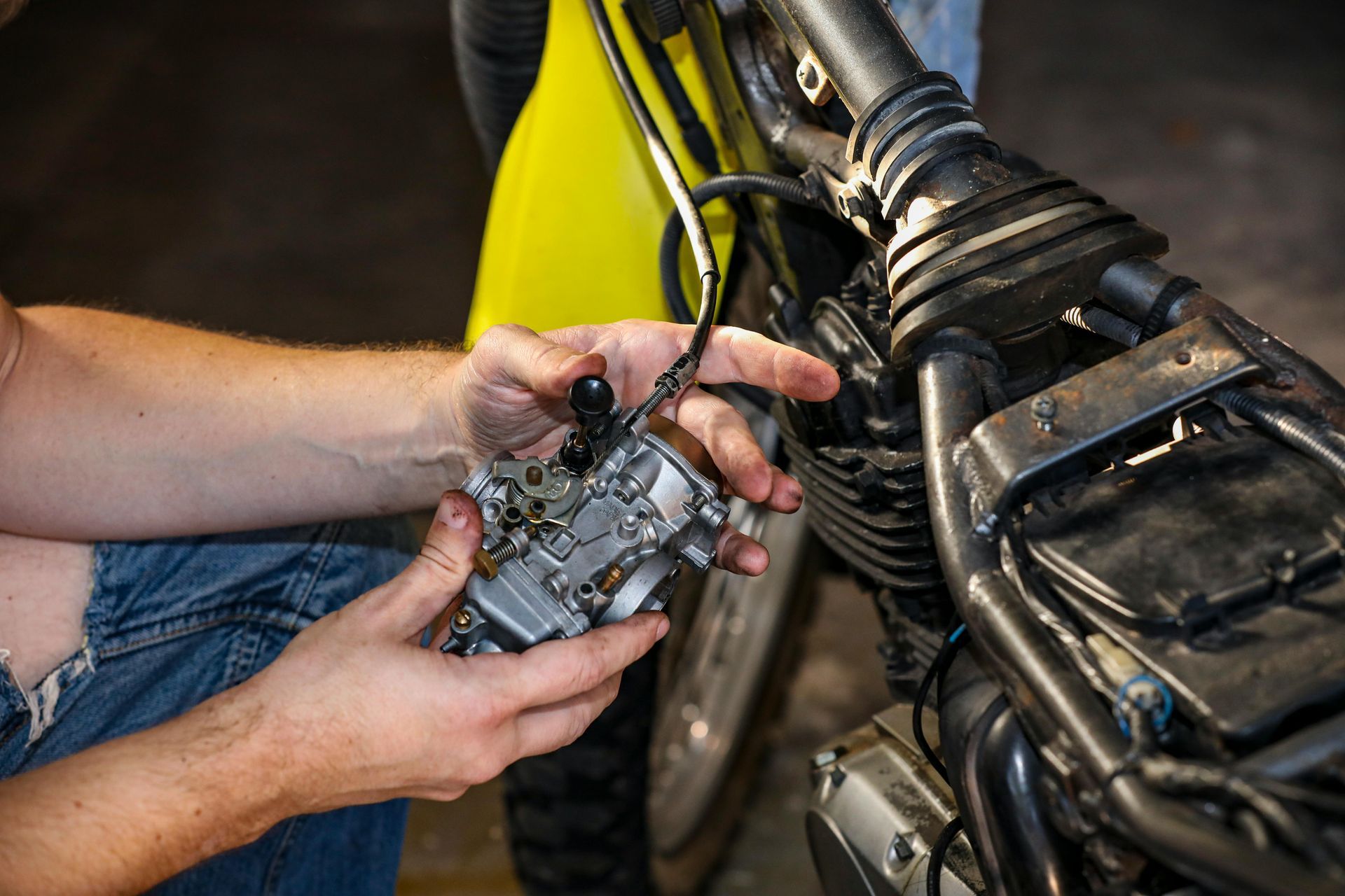 A pair of hands holding a motorcycle carburetor with a throttle cable attached.