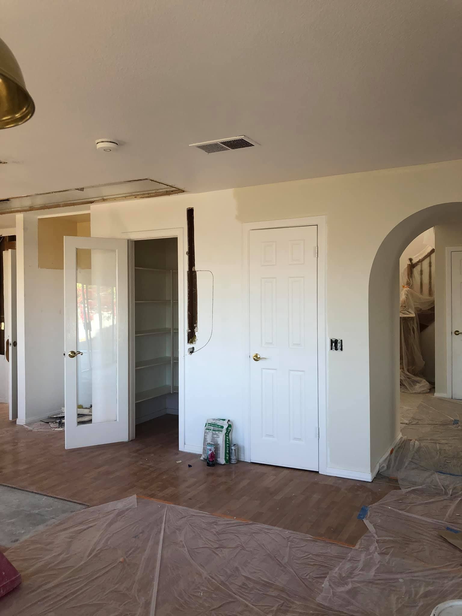 A living room with white walls and hardwood floors is being painted.
