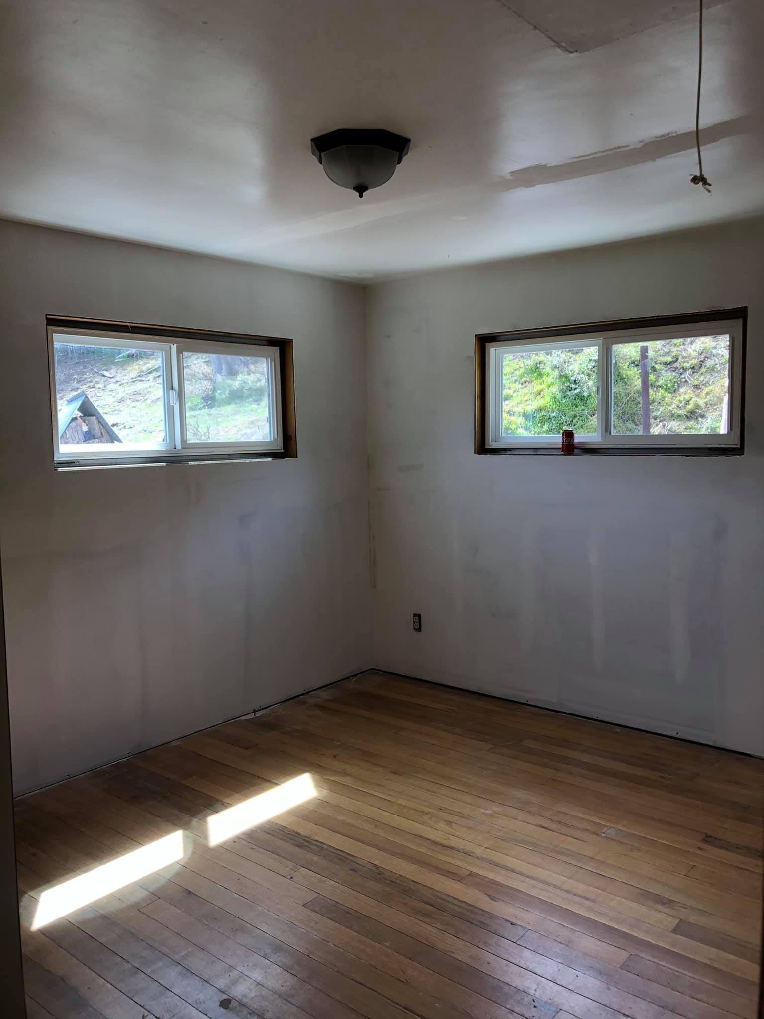 An empty room with wooden floors and two windows.