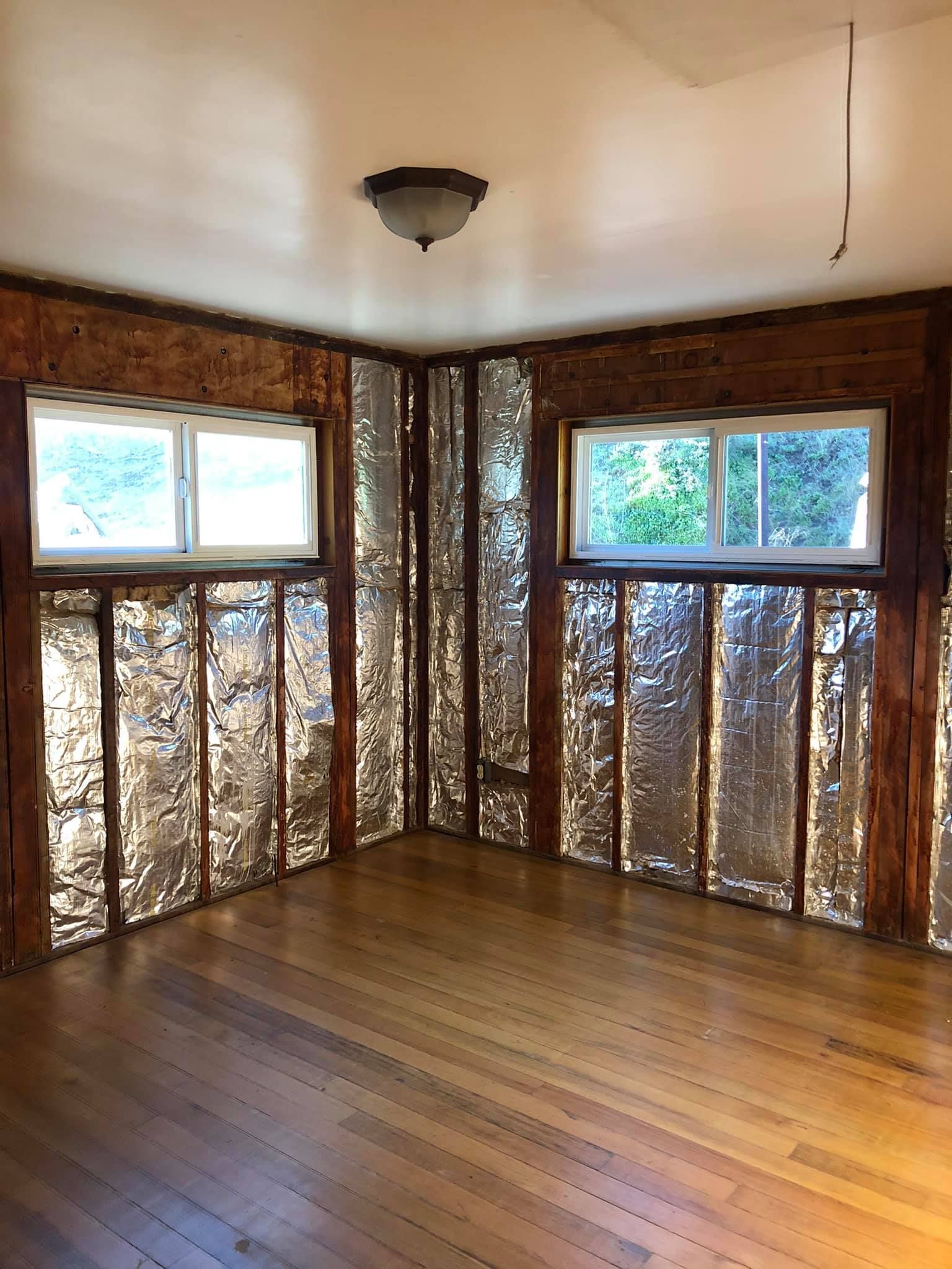 An empty room with wooden floors and aluminum foil on the walls.