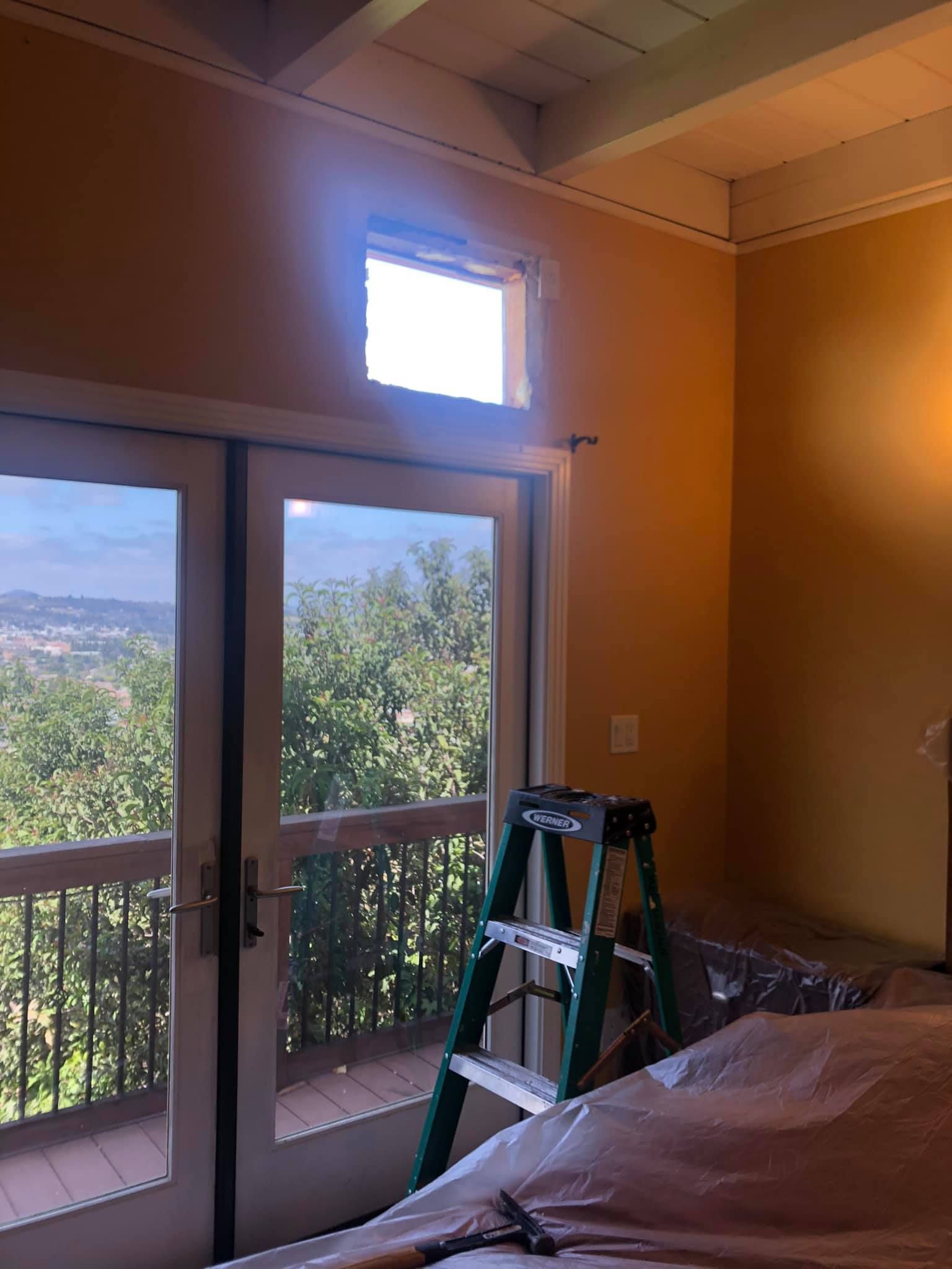 A bedroom with a bed and a ladder in front of a window.