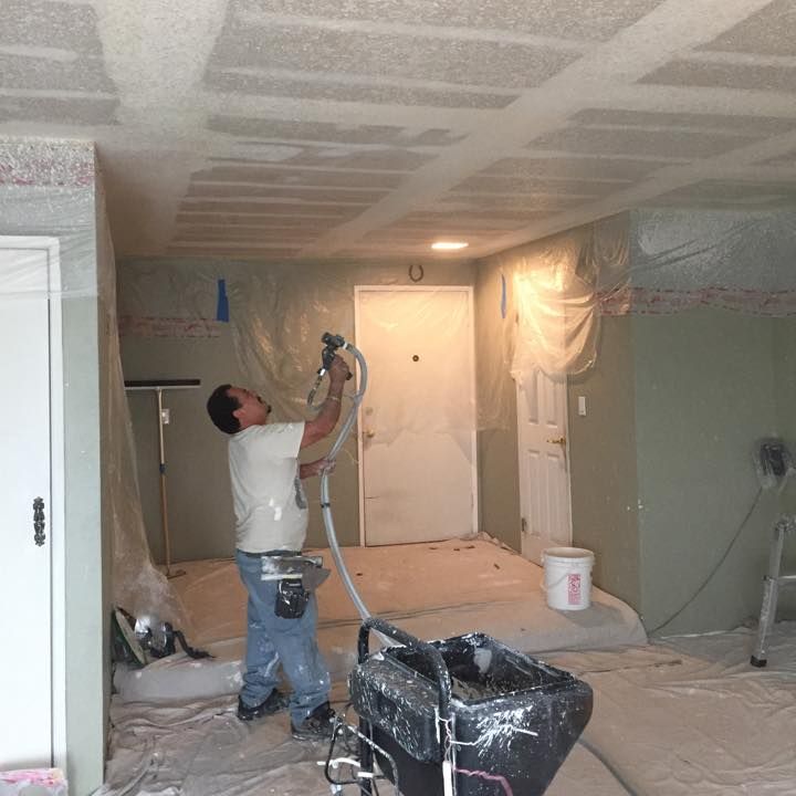A man is painting the ceiling of a room with a sprayer