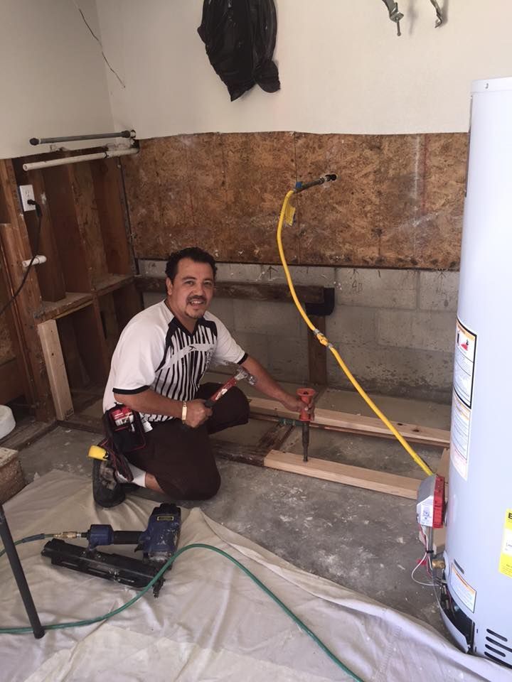 A man is kneeling down in a room next to a water heater.