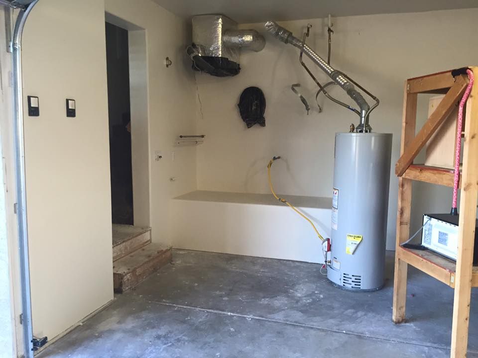 An empty garage with a water heater and a wooden shelf