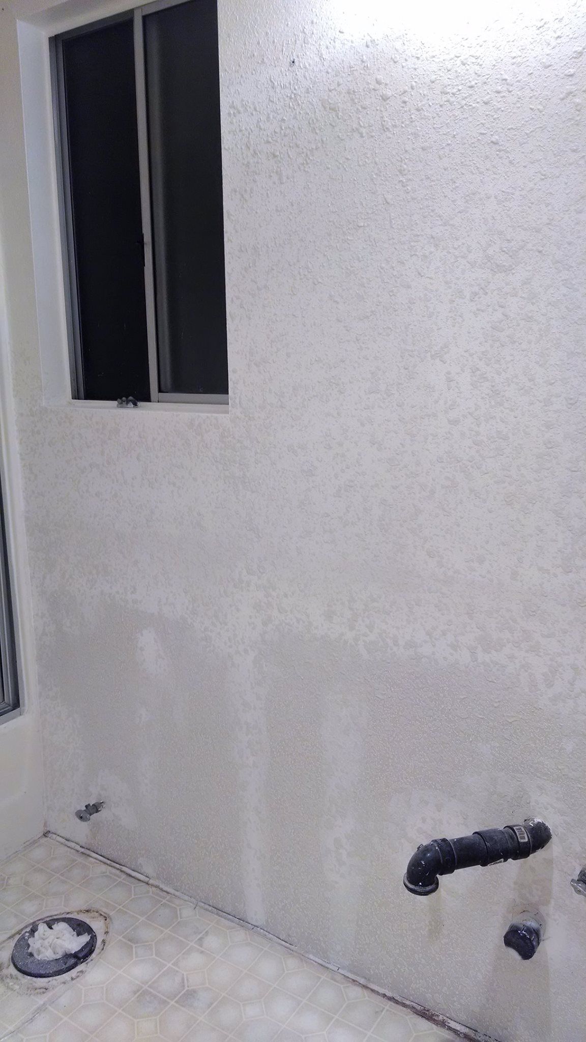 A white wall with a window in the corner of a room.