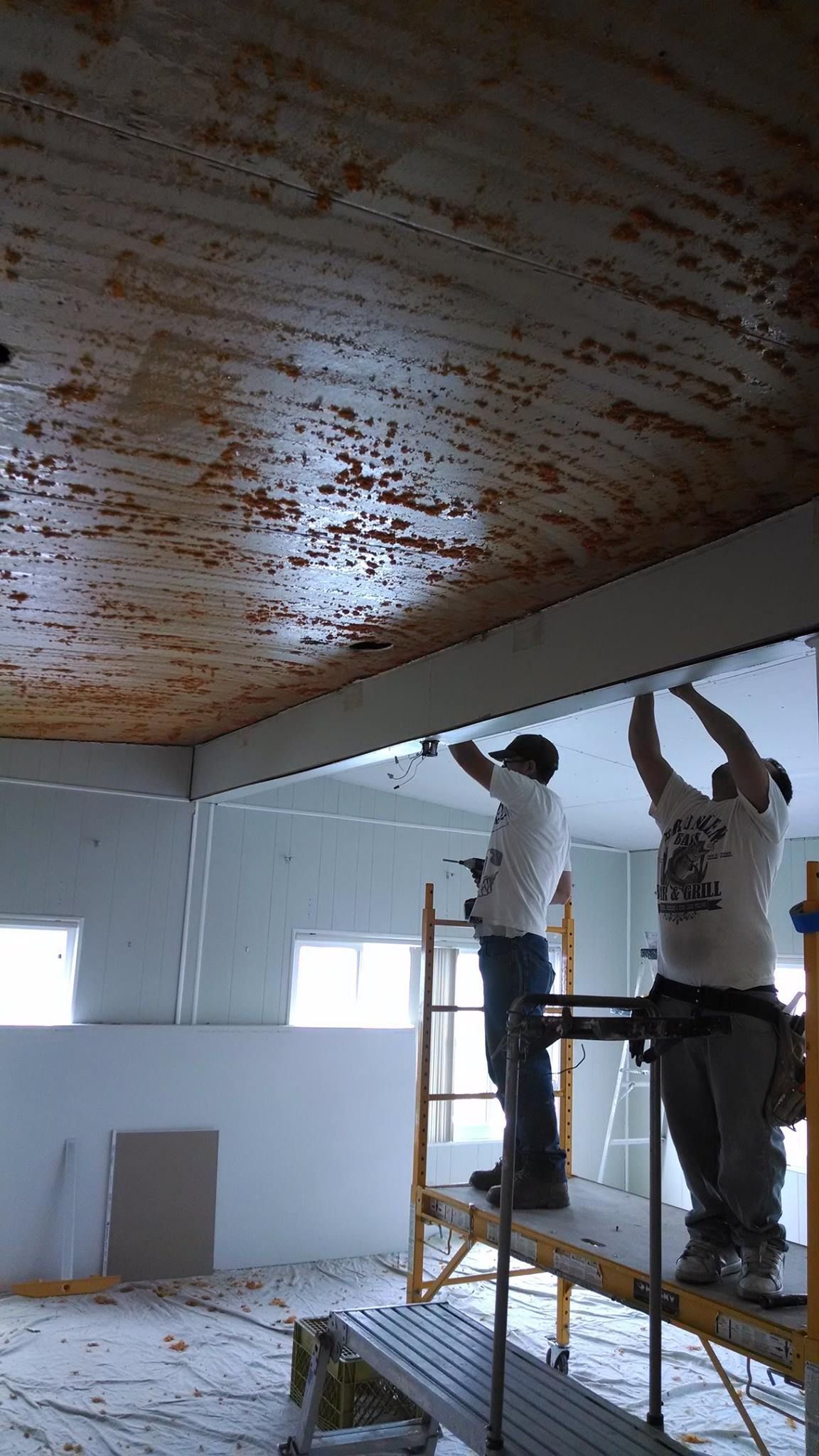 Two men are working on the ceiling of a building.