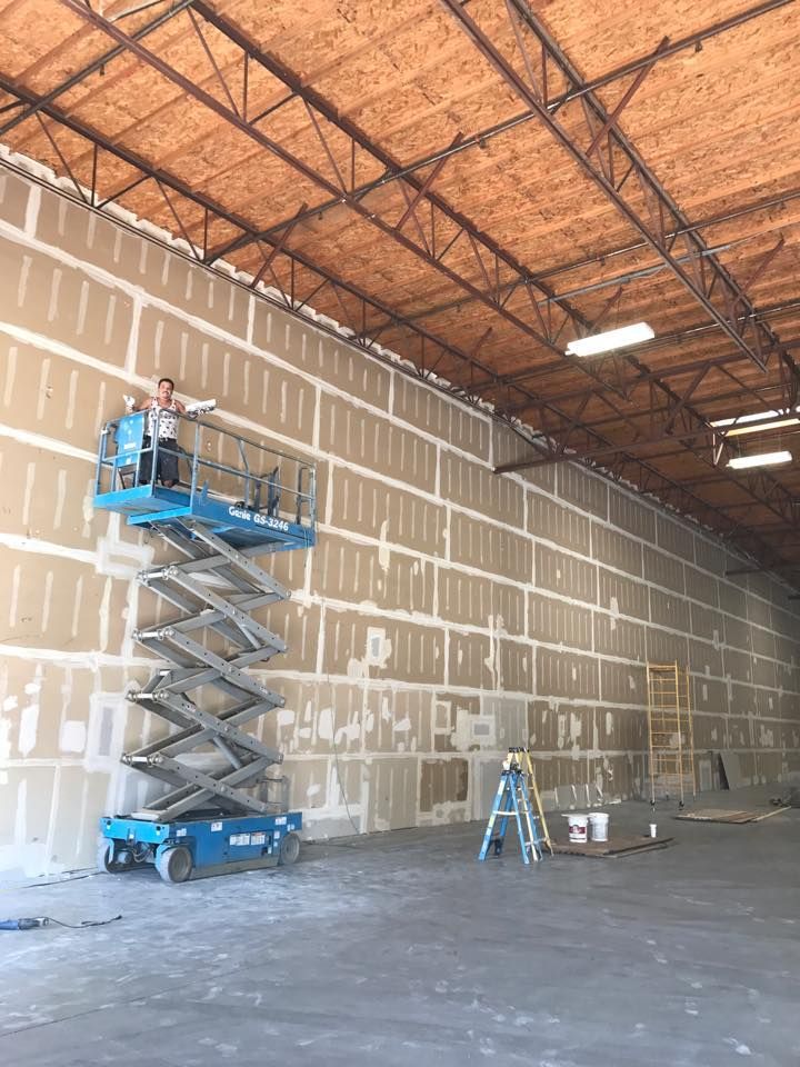 A man is standing on a scissor lift in front of a large wall.