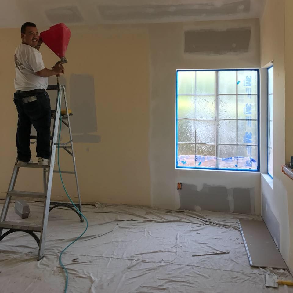 A man is standing on a ladder in a room holding a red cone.
