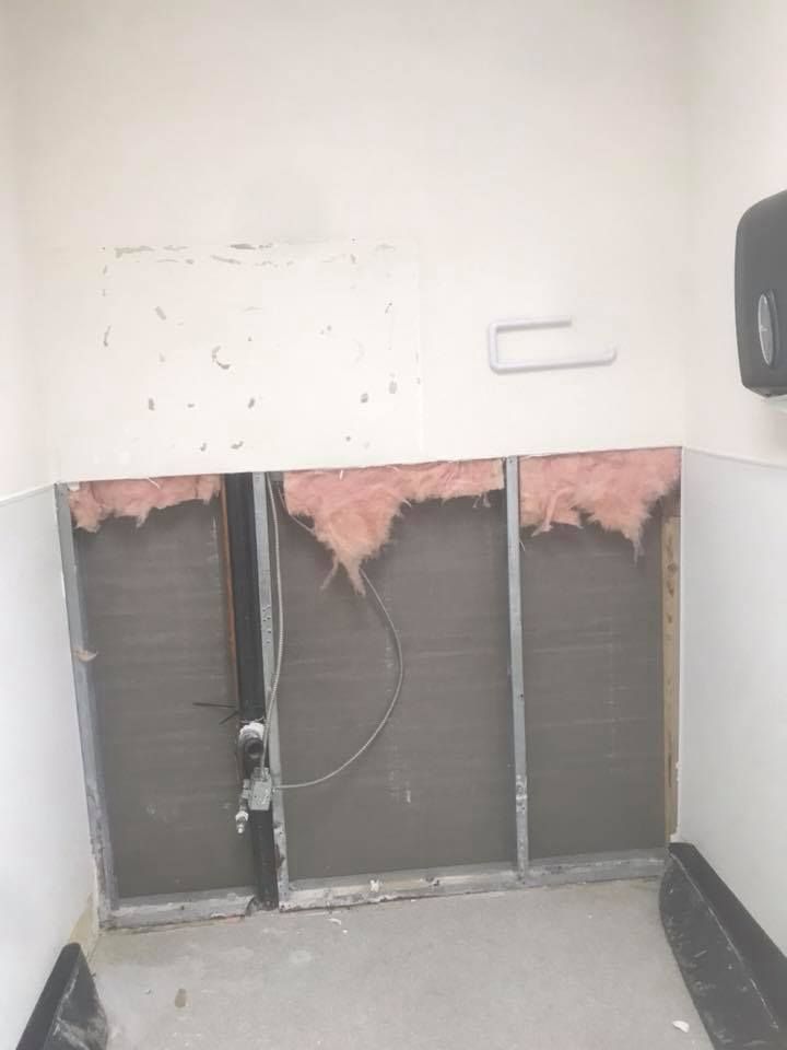 A bathroom with a hole in the wall and a paper towel dispenser.