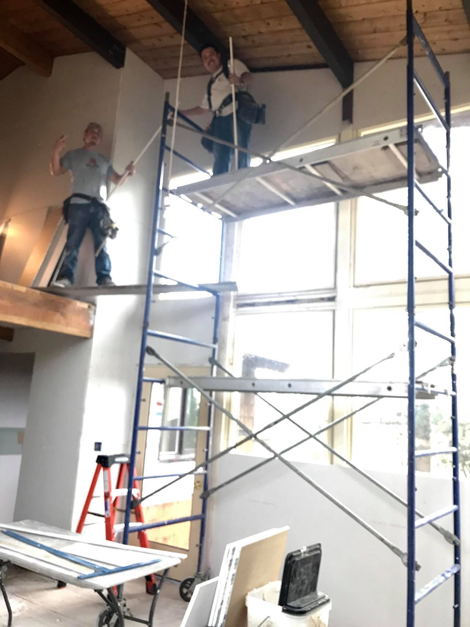 Two men are working on a scaffolding in a room.