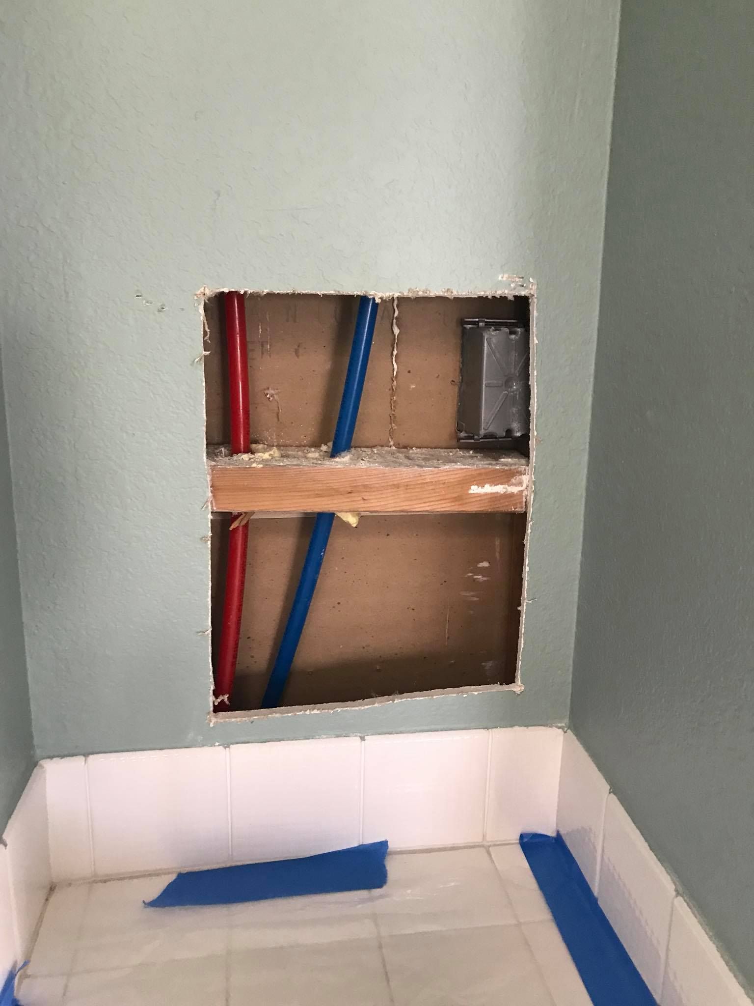 A bathroom with a hole in the wall and pipes coming out of it.