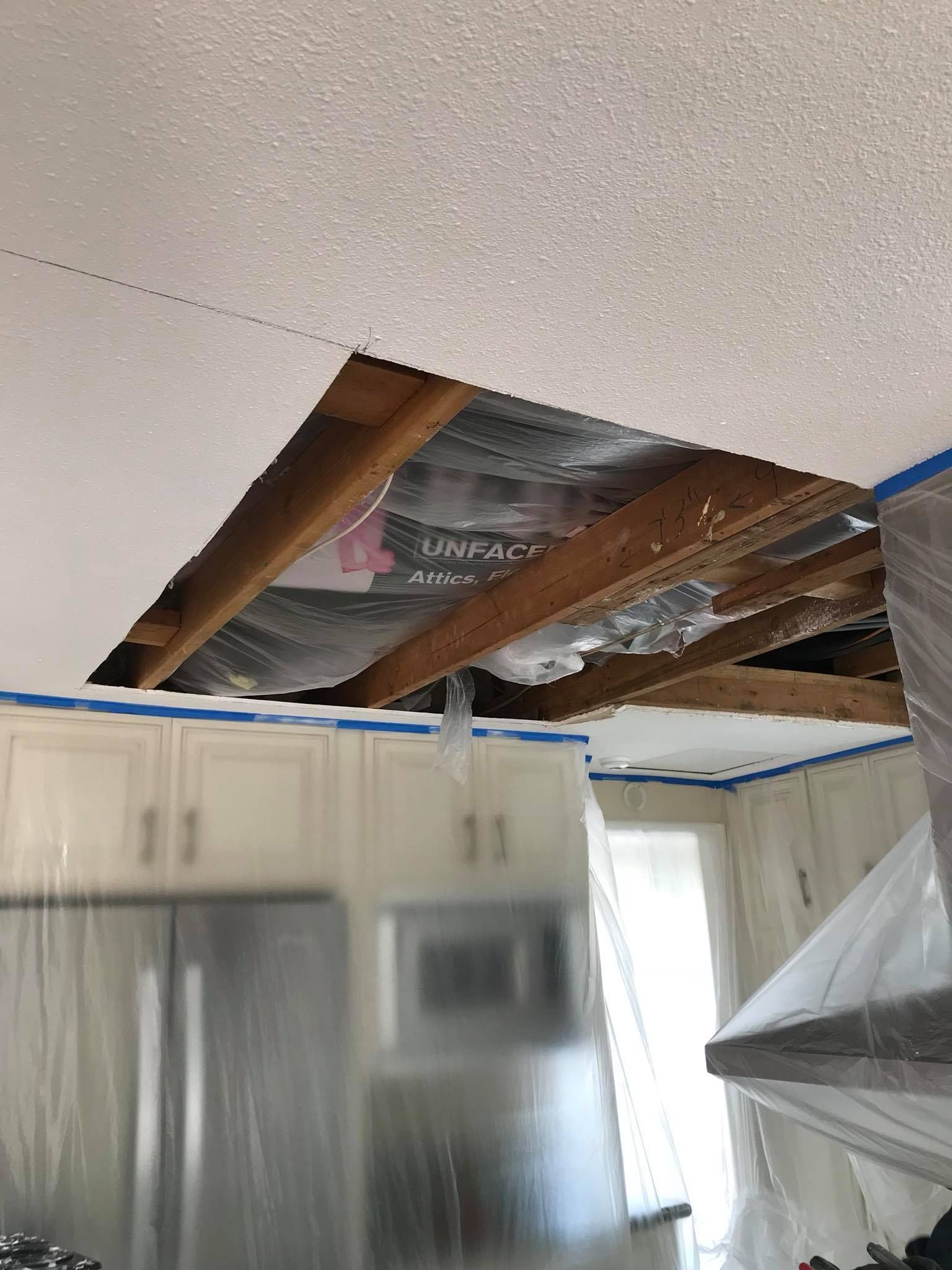 A kitchen with a hole in the ceiling and a ceiling fan.