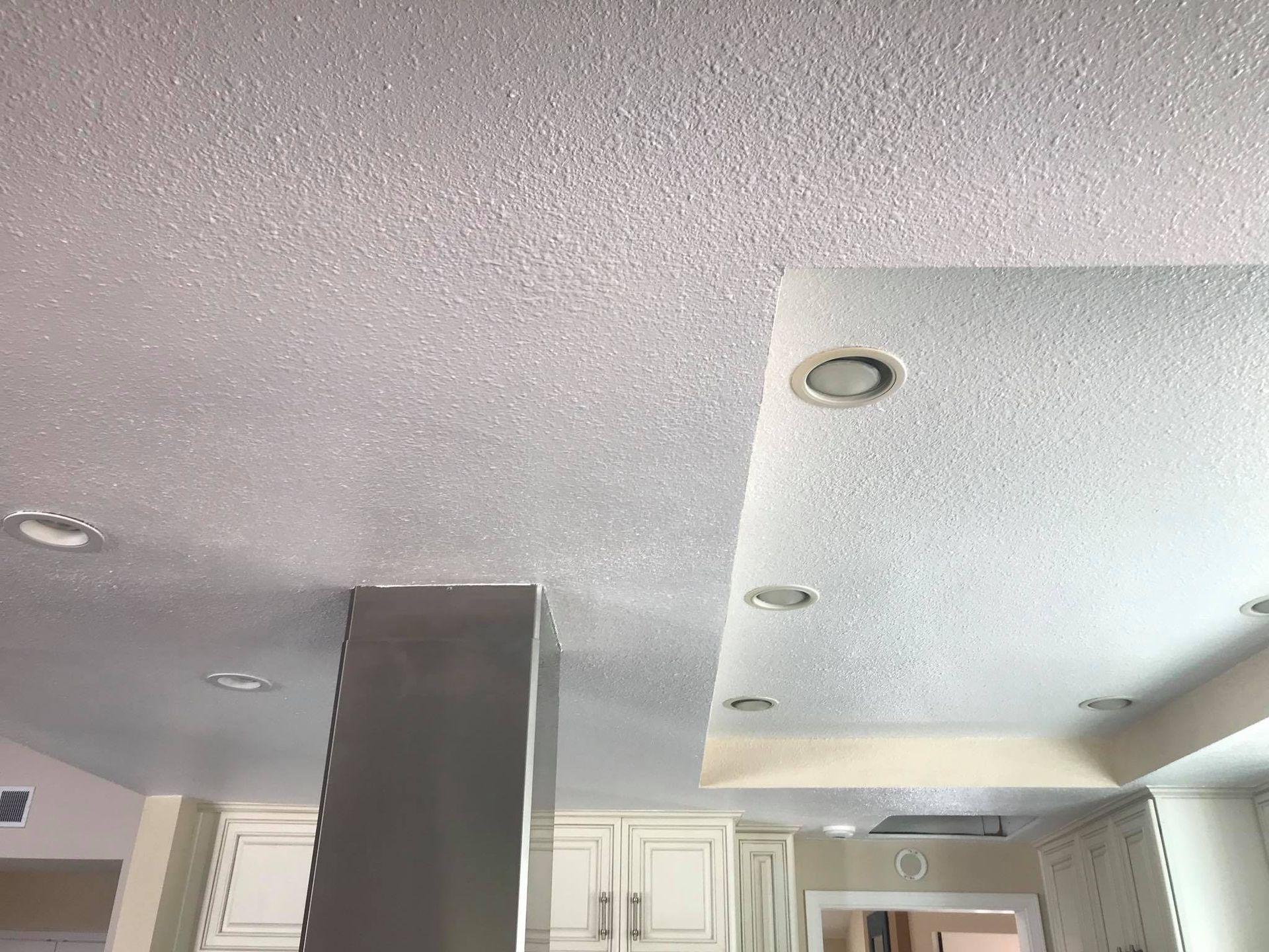 A kitchen with a white ceiling and a stainless steel hood.
