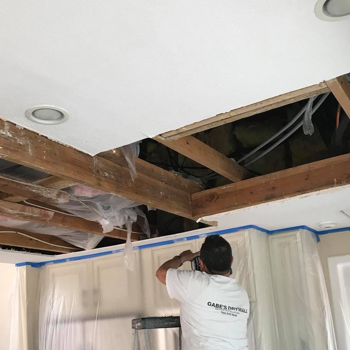 A man in a white shirt is working on a ceiling.