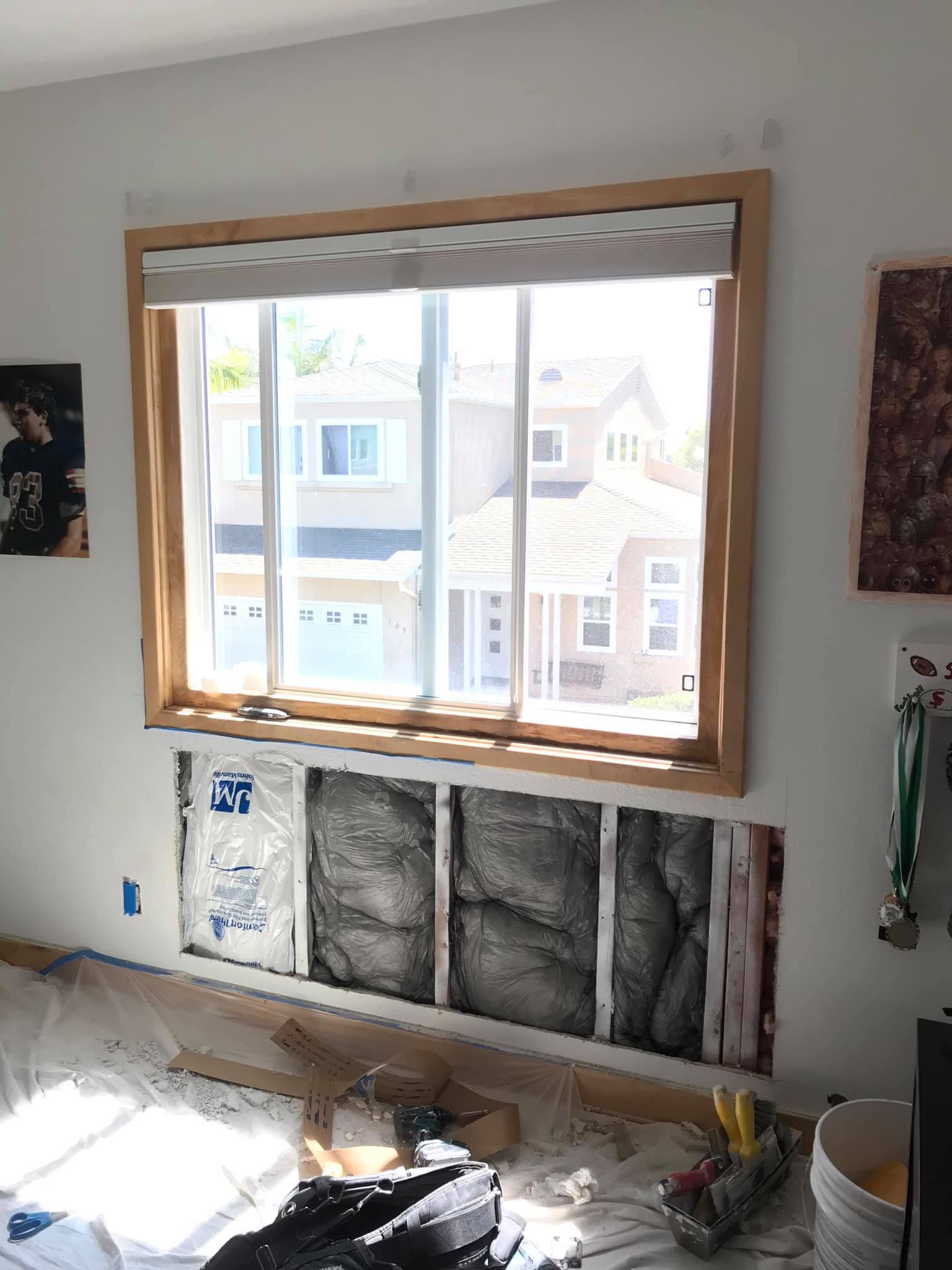 A room with a large window and a bucket of paint on the floor.