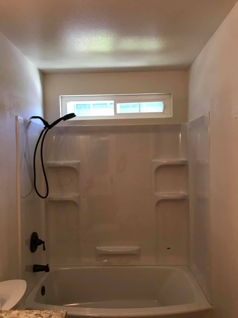 A bathroom with a bathtub , shower , and window.