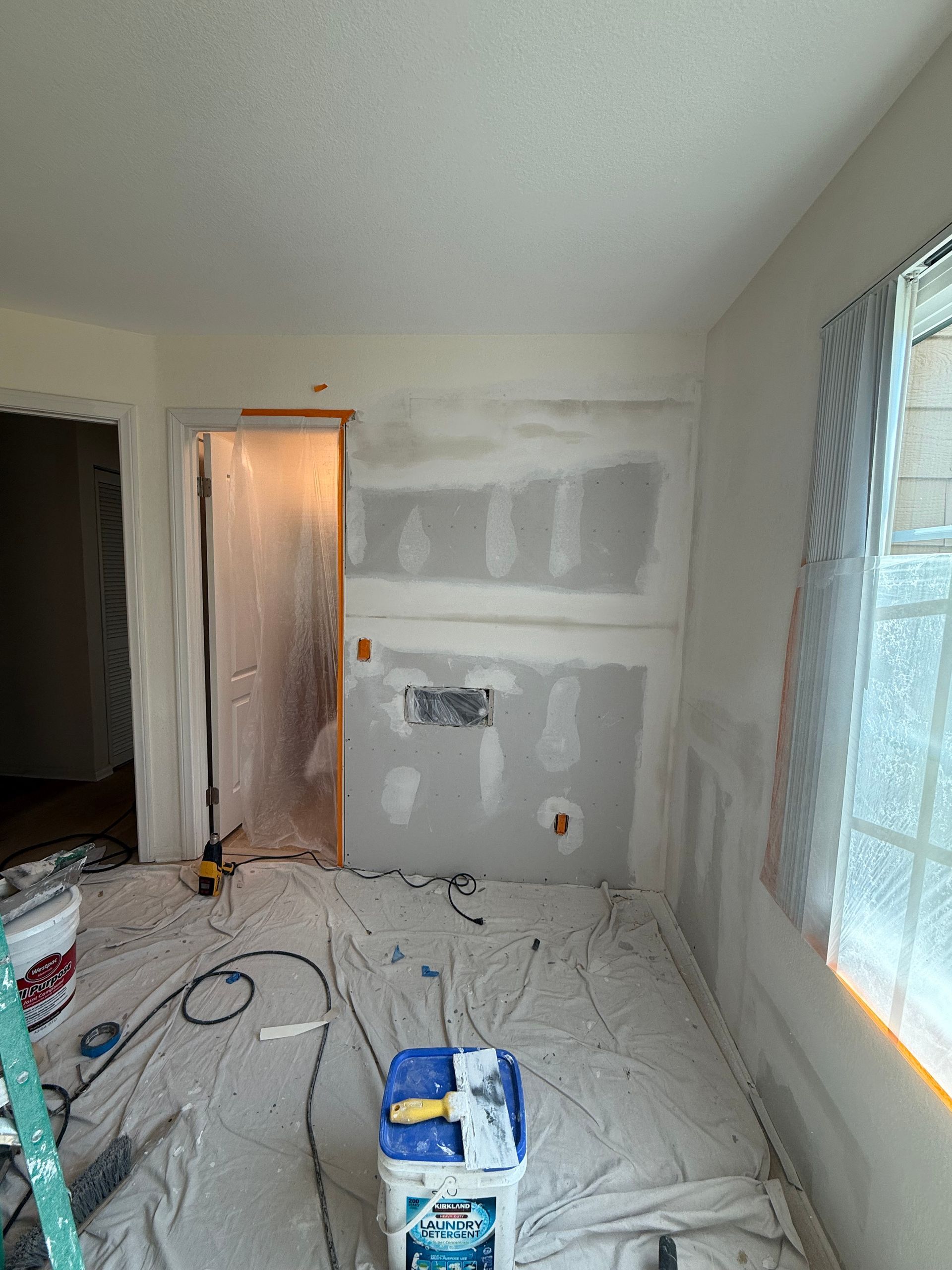 Room renovation in progress; drywall installed on a wall with electrical outlets, covered with plastic.