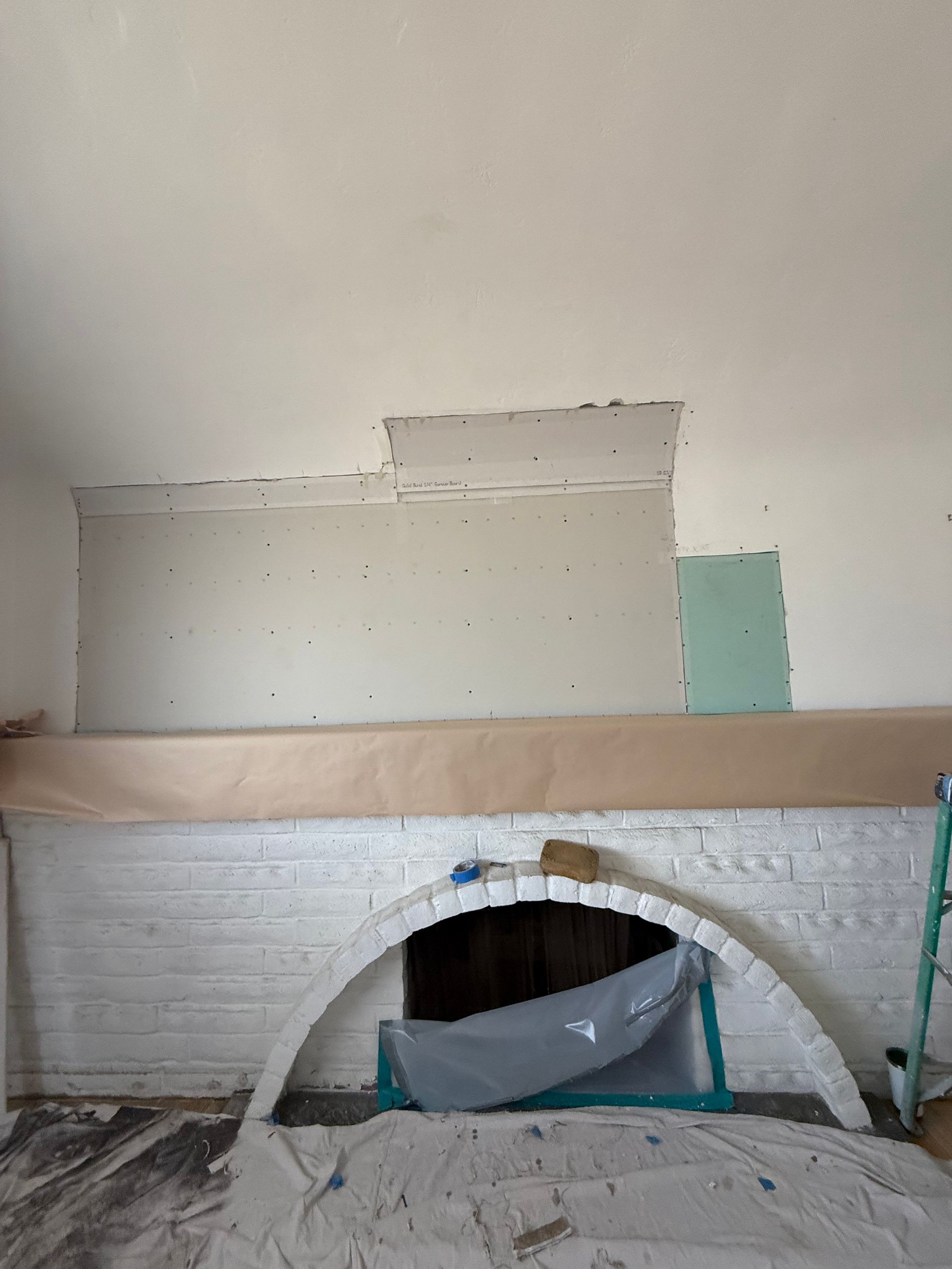 A partially renovated fireplace with white brick and arch, drywall patches on the wall, and protective coverings.
