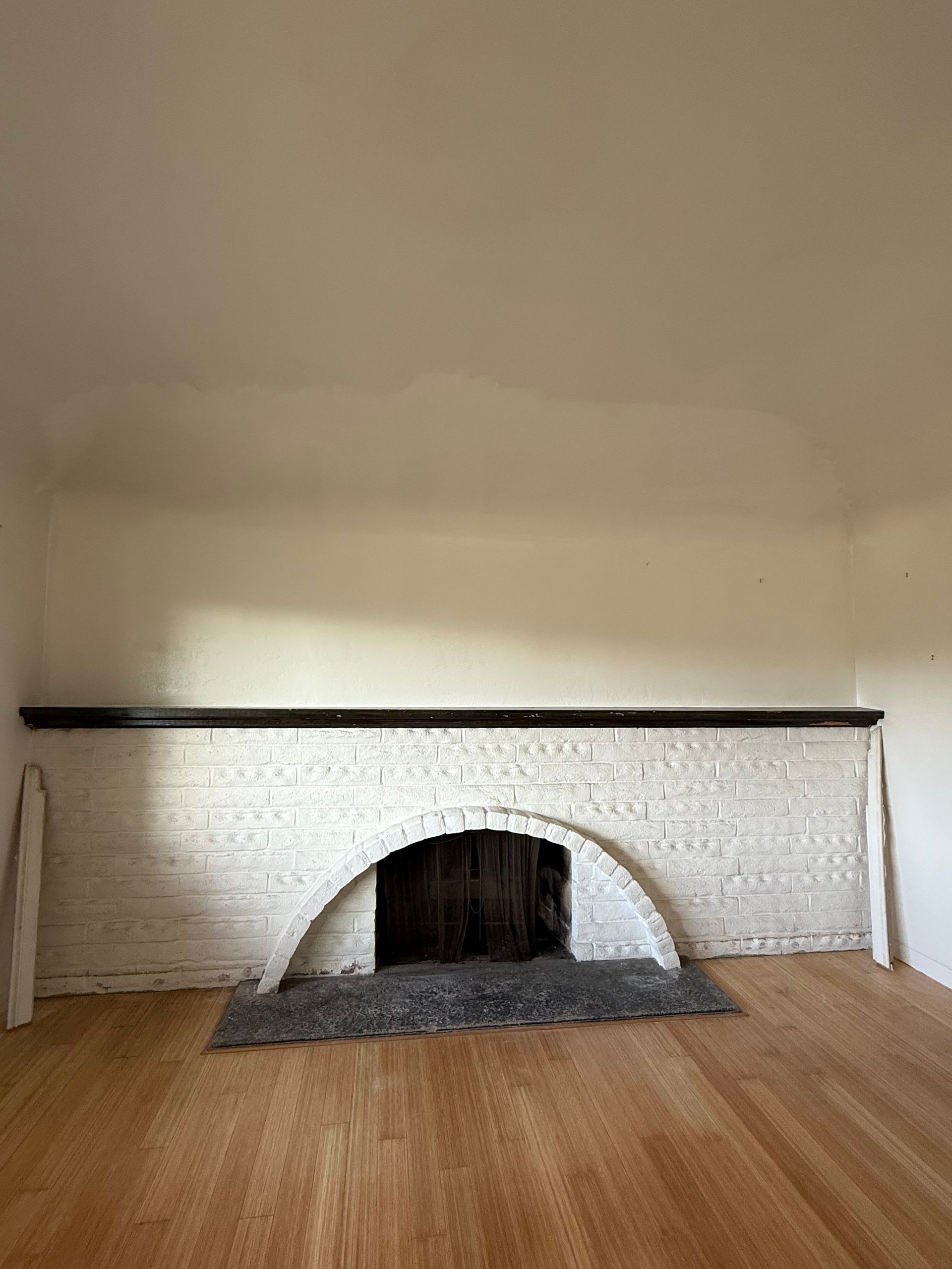 Fireplace with white brick, arched opening, and dark wood mantel. A dark mat sits in front on a hardwood floor.