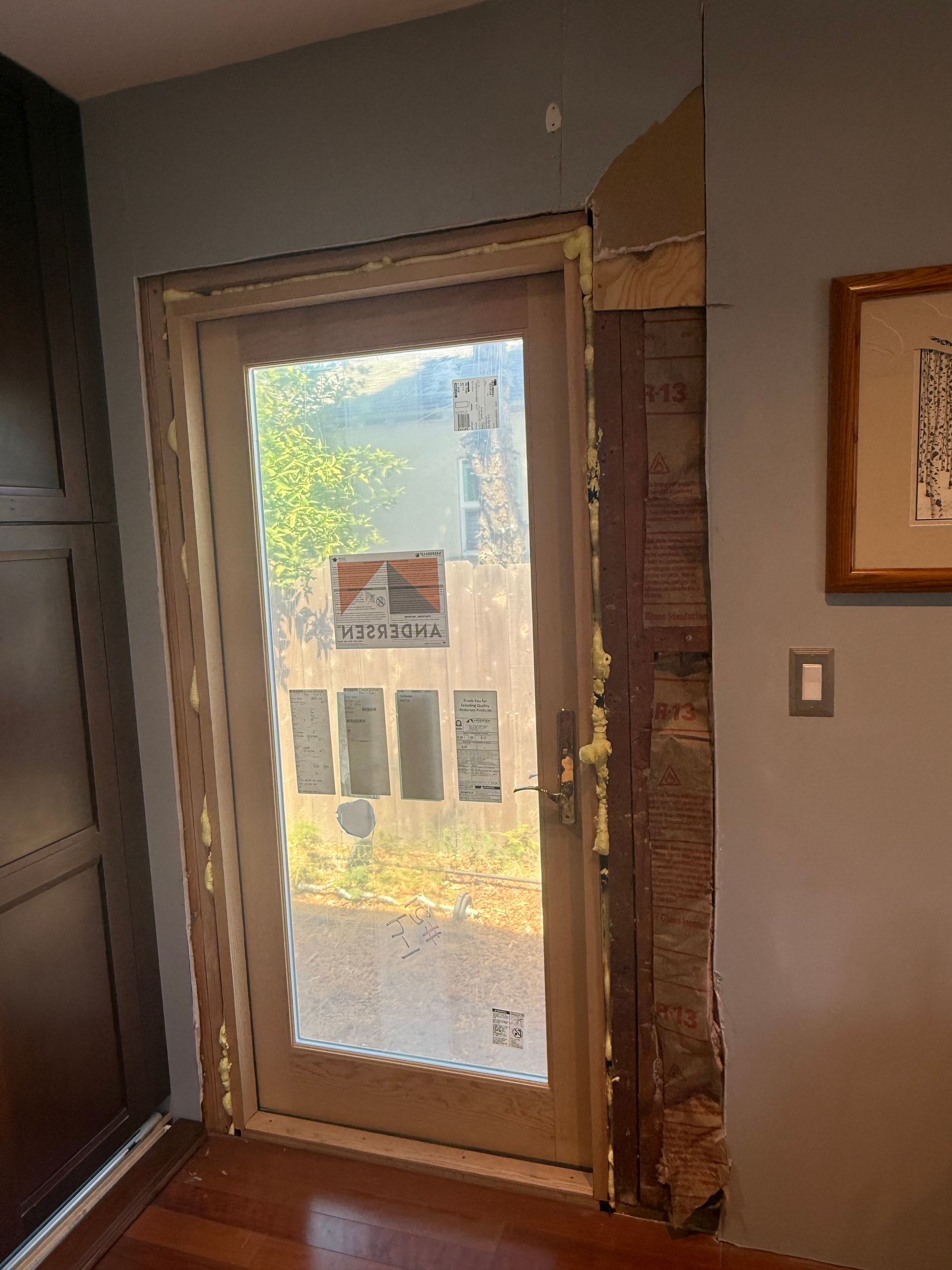 A door with a glass panel, looking out to a yard, surrounded by light-colored trim. The door has notices taped to the glass.