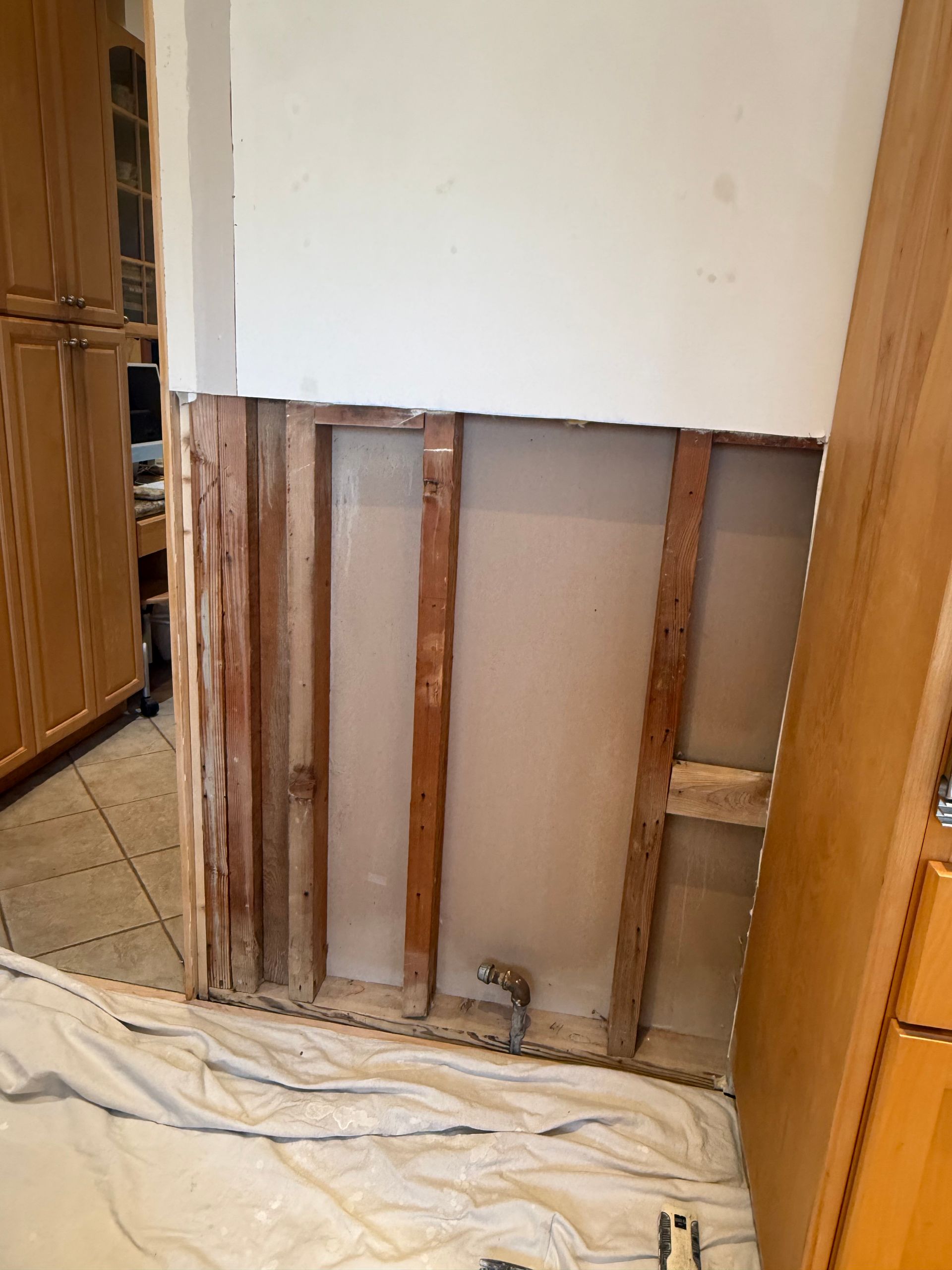 Wall studs exposed after drywall removal. Beige wall studs, white insulation, and a silver pipe are visible.