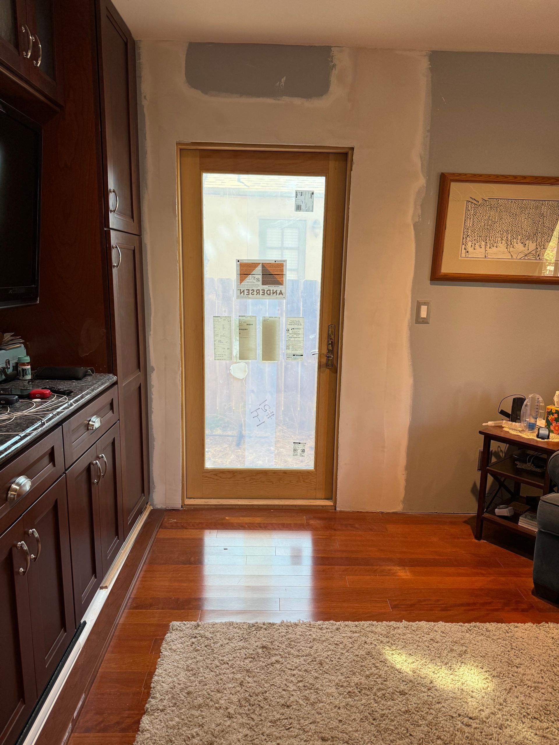Wooden door framed by unfinished walls in a room with dark wood cabinetry and flooring. Light shines through the frosted glass door.