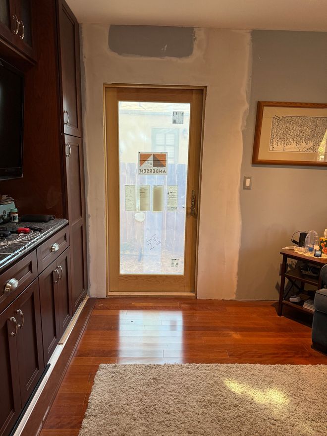 Wooden door framed by unfinished walls in a room with dark wood cabinetry and flooring. Light shines through the frosted glass door.