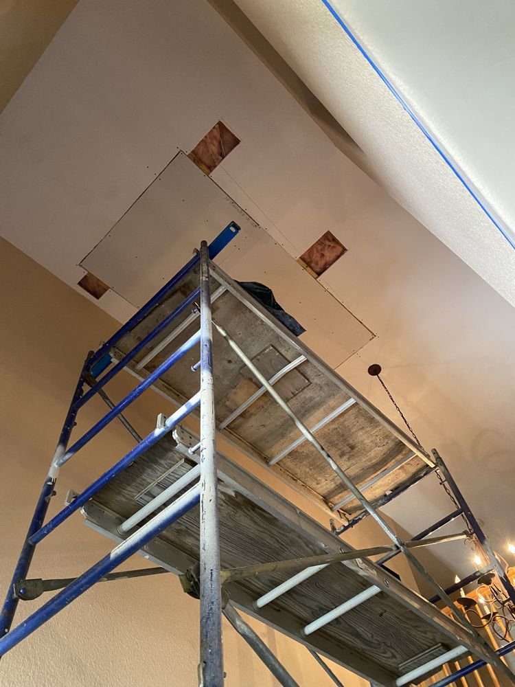 A person is standing on a scaffolding looking up at the ceiling.