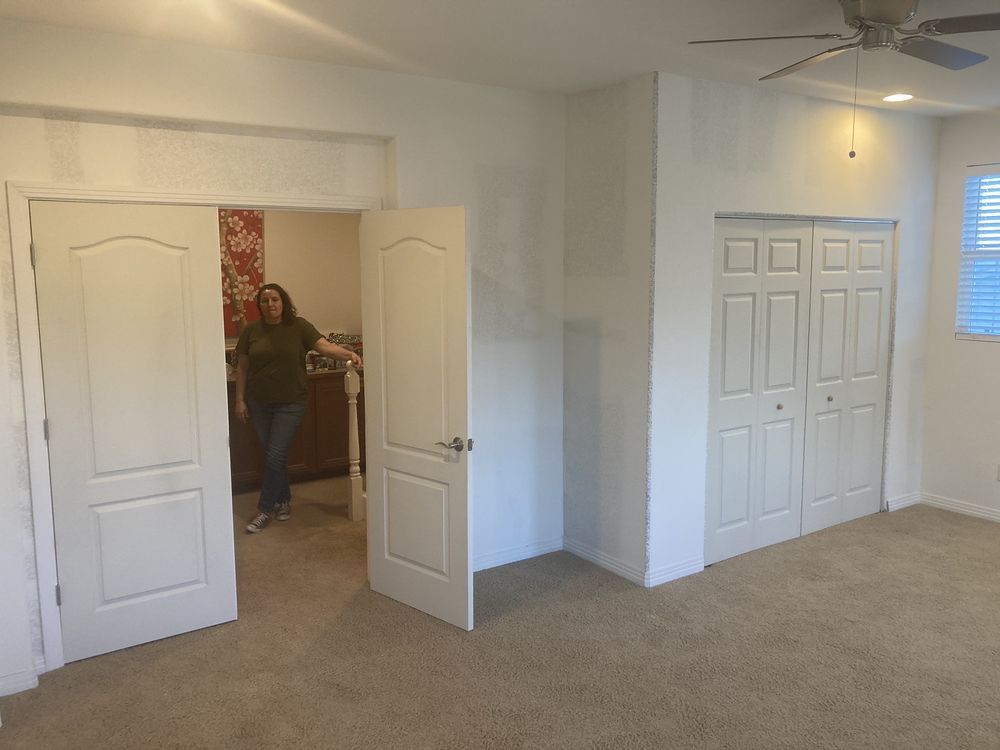 A woman is standing in an empty bedroom with a ceiling fan.