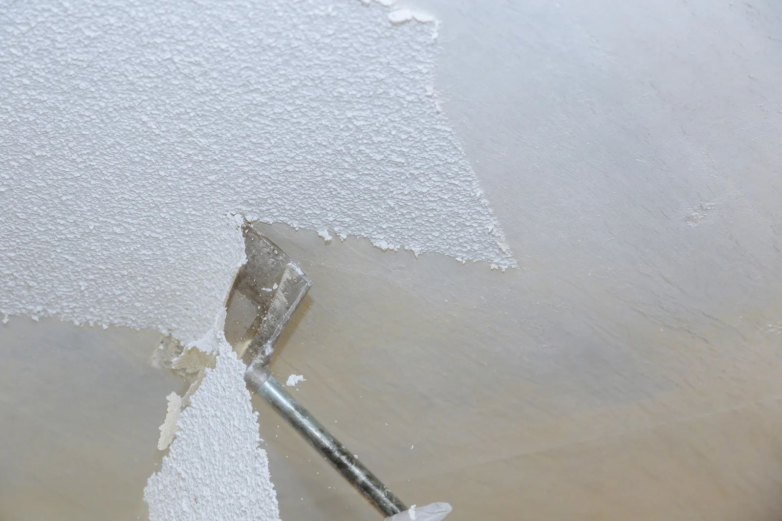 Paint roller applying white paint to a ceiling edge with a patch of peeled paint