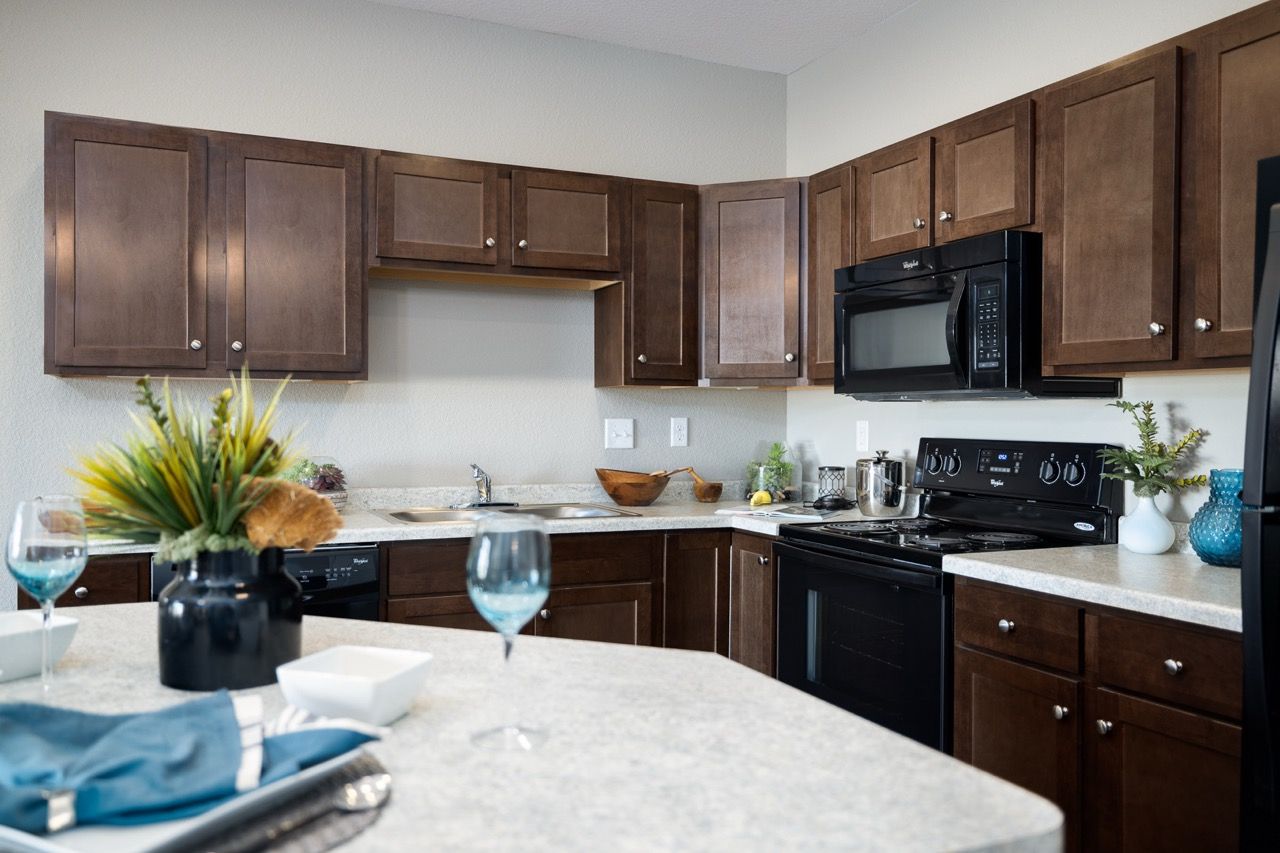 Apartment kitchen with dark wood cabinets, black stove and microwave, beige countertops, and a breakfast island.