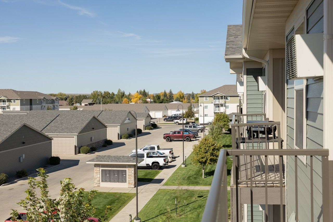 Balcony view of a multi-building apartment community with garages, parking, and green lawns.