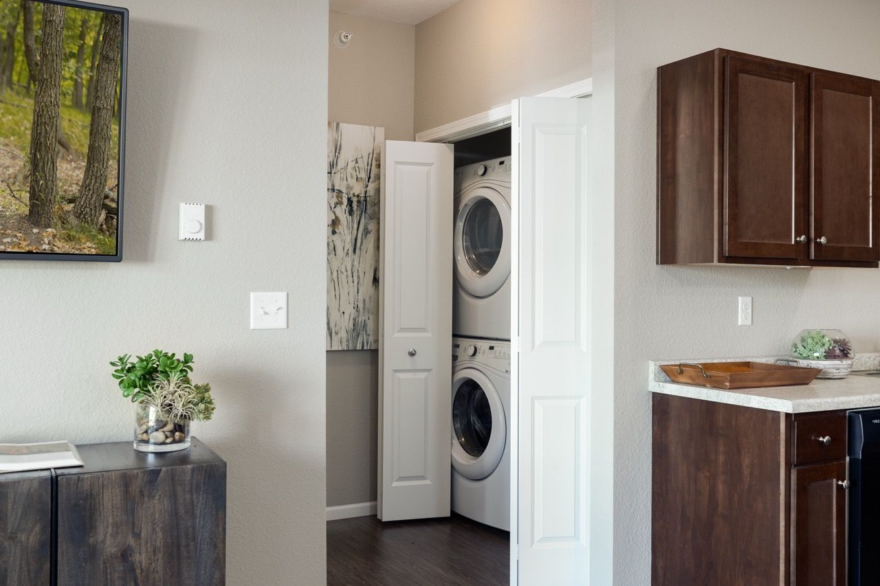 In-unit laundry closet with stacked washer and dryer beside kitchen cabinets.