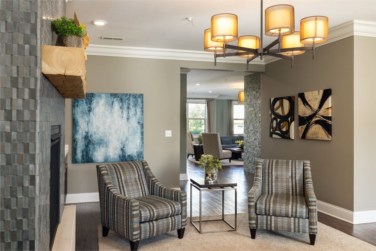 Living room in an apartment with two patterned armchairs, a stone fireplace, and wall art.