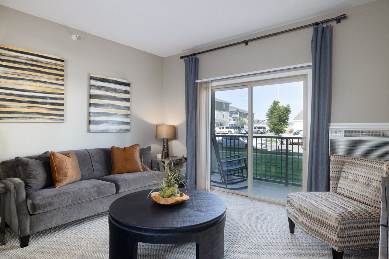 Living room in an apartment with gray sofa, chairs, and a sliding glass door to a balcony.