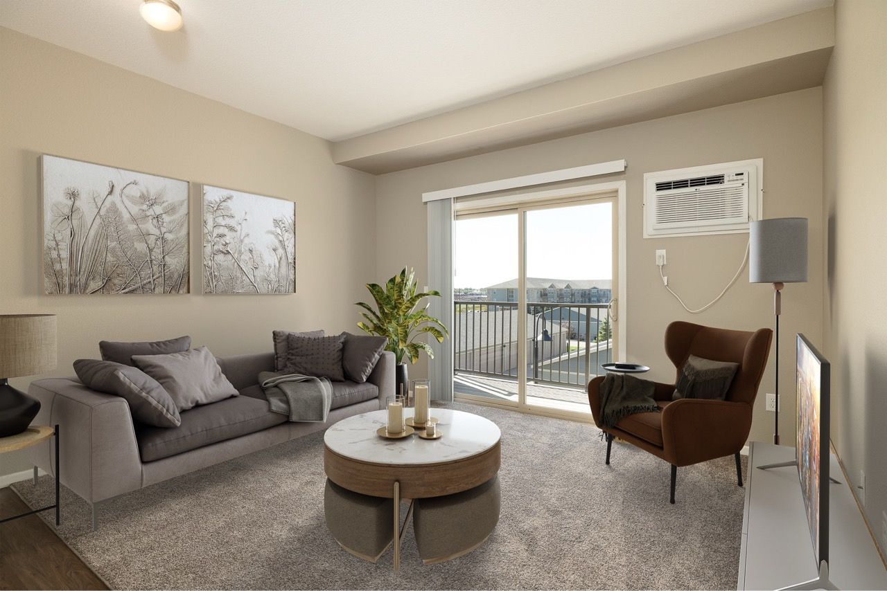 Living room in an apartment with a gray sofa, round coffee table, chair, TV, and sliding balcony doors.