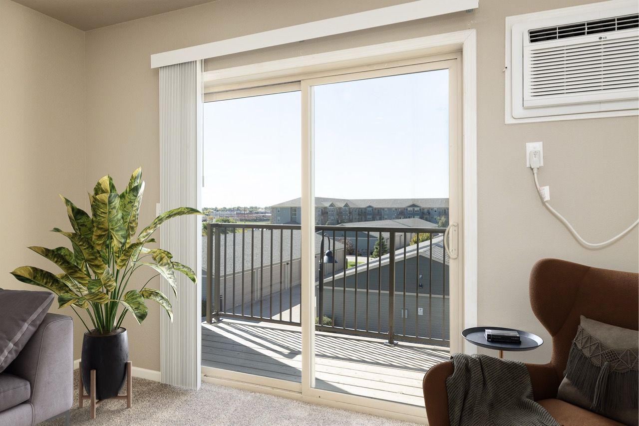 Living room with sliding glass door to a balcony, plant, and brown chair.
