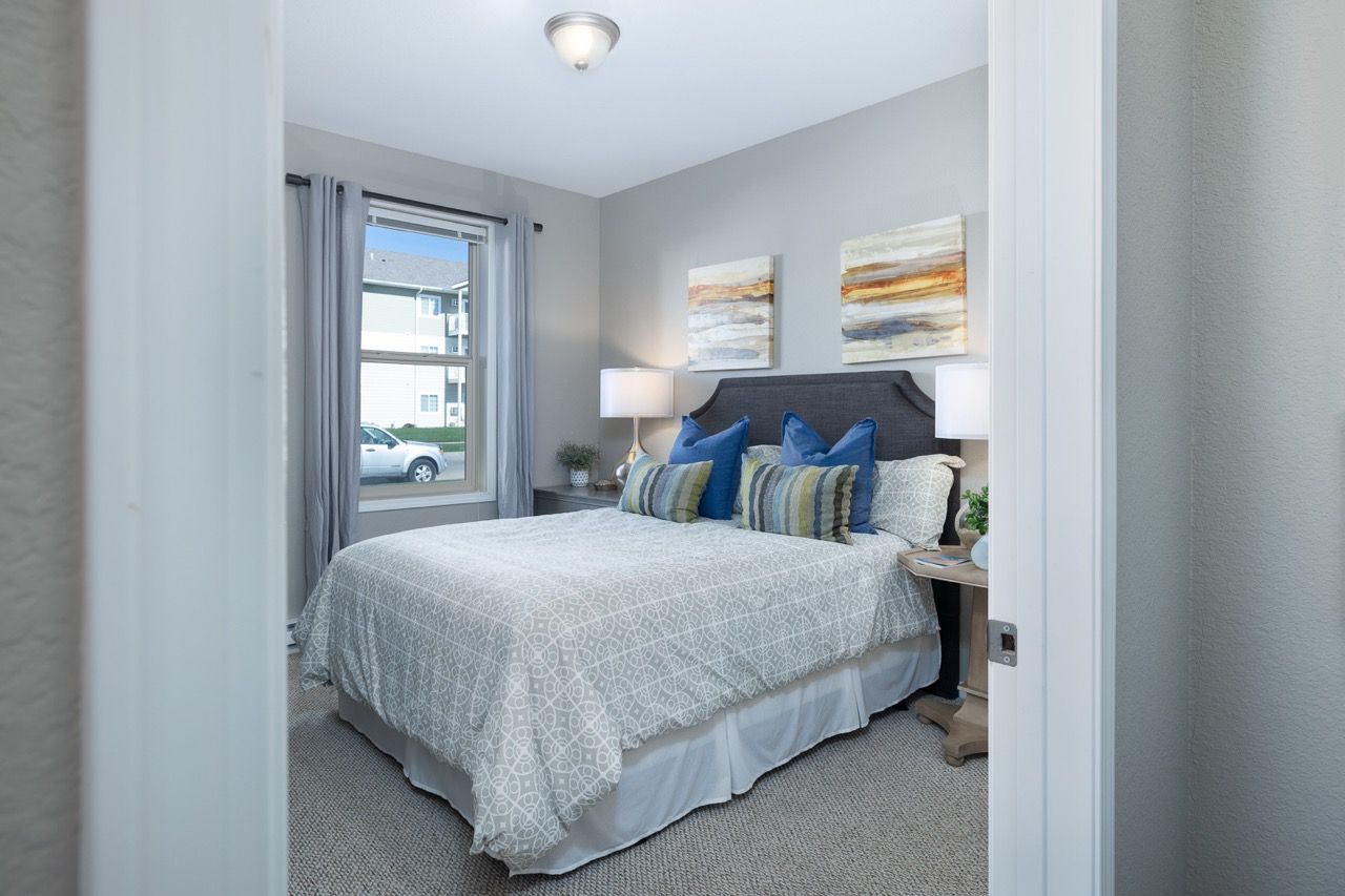 Bedroom in an apartment with a queen bed, two nightstands, lamps, and a window with curtains.