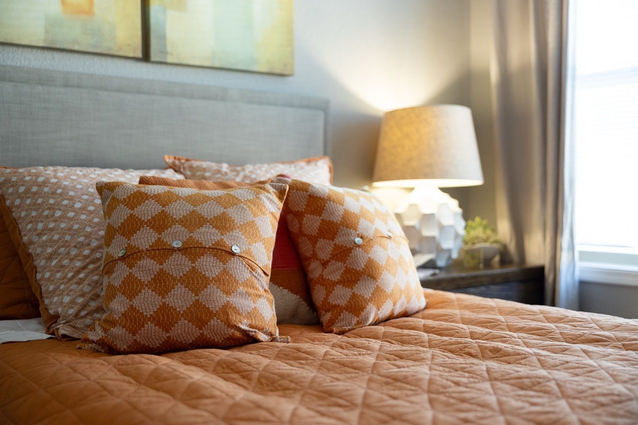 Modern apartment bedroom with an orange-patterned quilt and matching pillows on the bed.