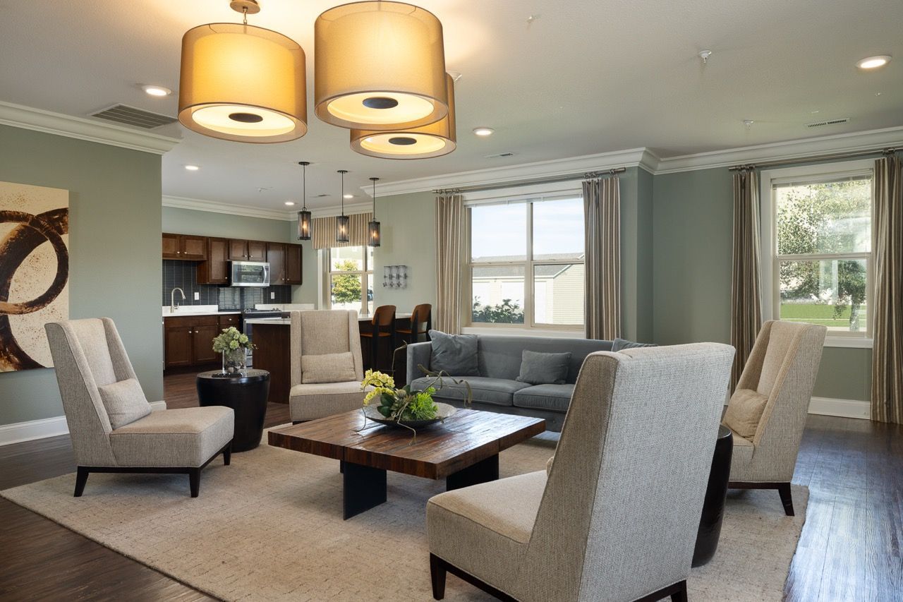 Bright apartment living room with beige chairs, a gray sofa, and a wooden coffee table near the kitchen.