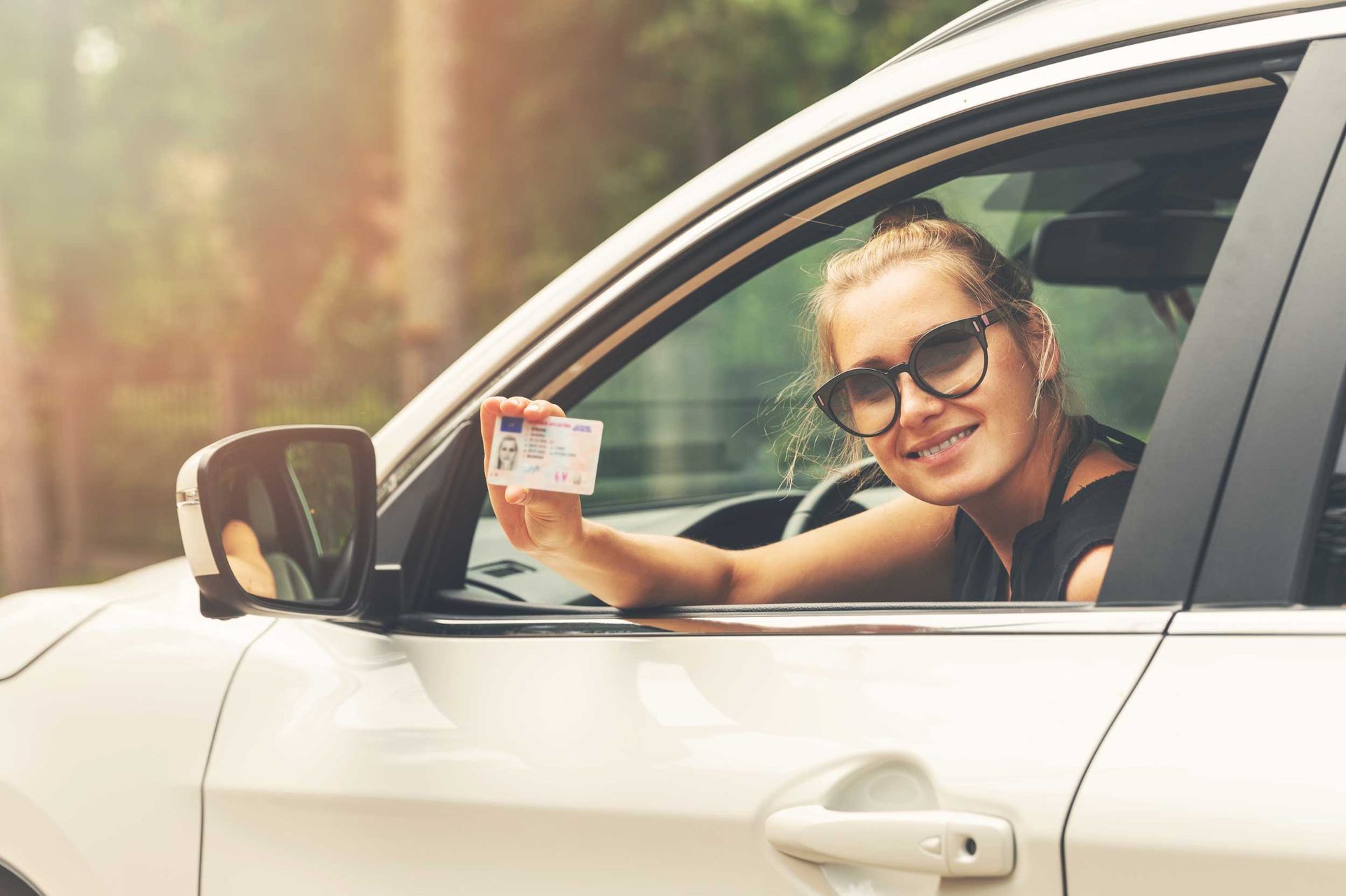 Driver sitting in a car and holding a license card out the window during a lesson.